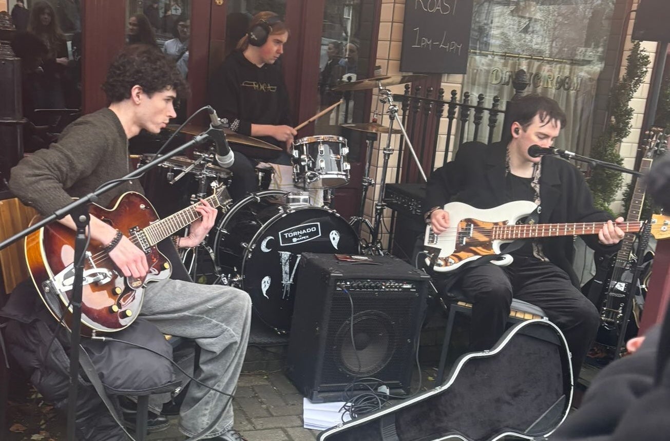 A band of musicians seated, playing outside a shop front.