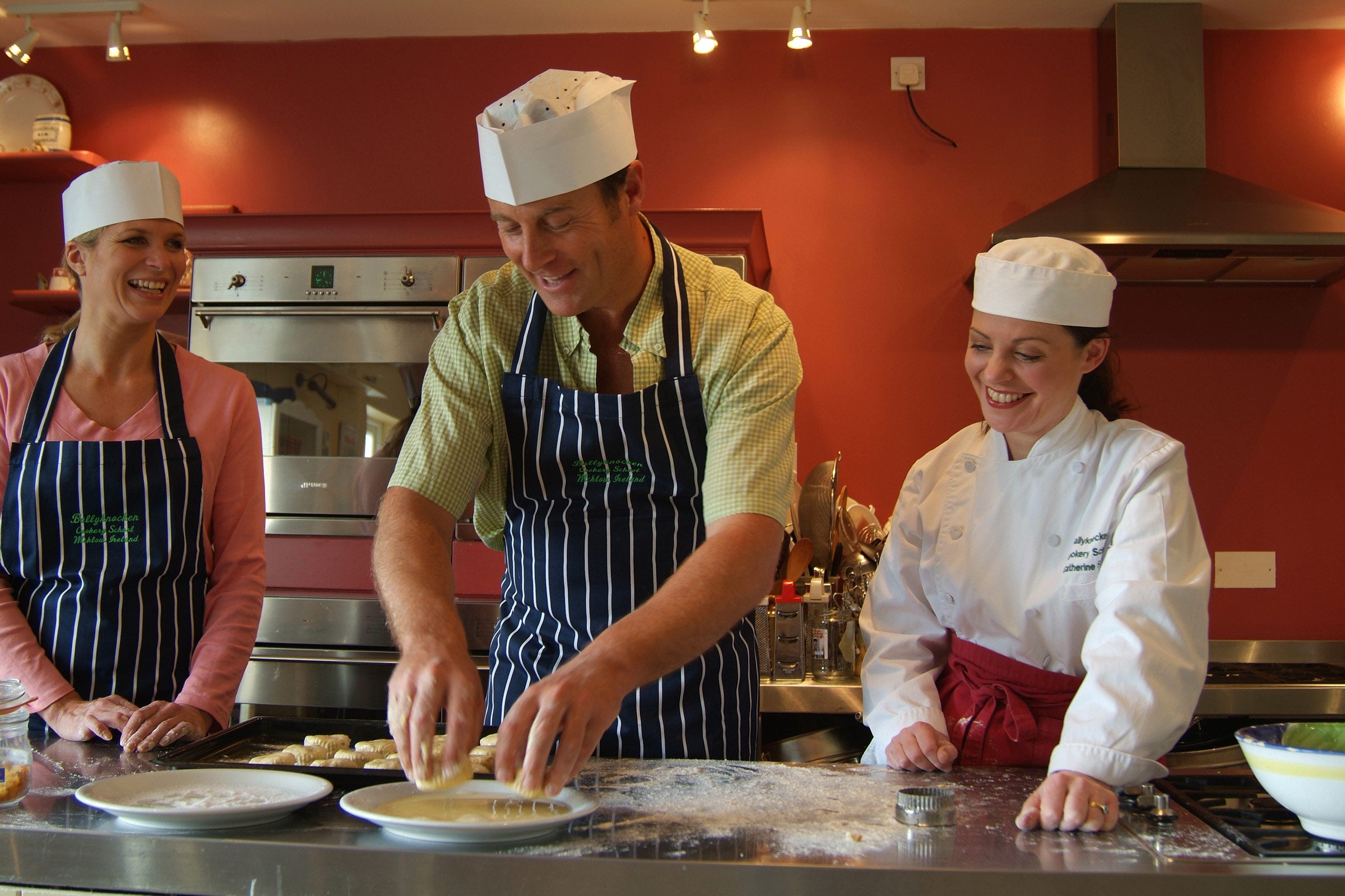 A chef showing two students how to cook in a red kitchen in Ballyknocken, County Wicklow