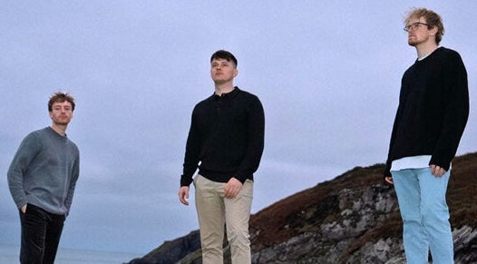 3 men standing apart outdoors with dull sky