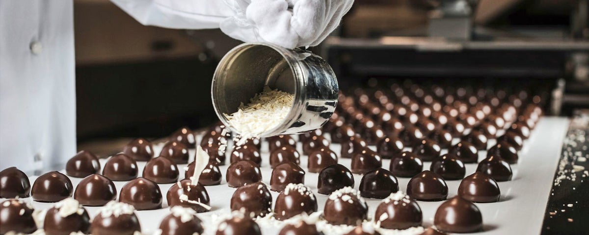 A row of chocolate sweets being sprinkled with flakes during manufacturing