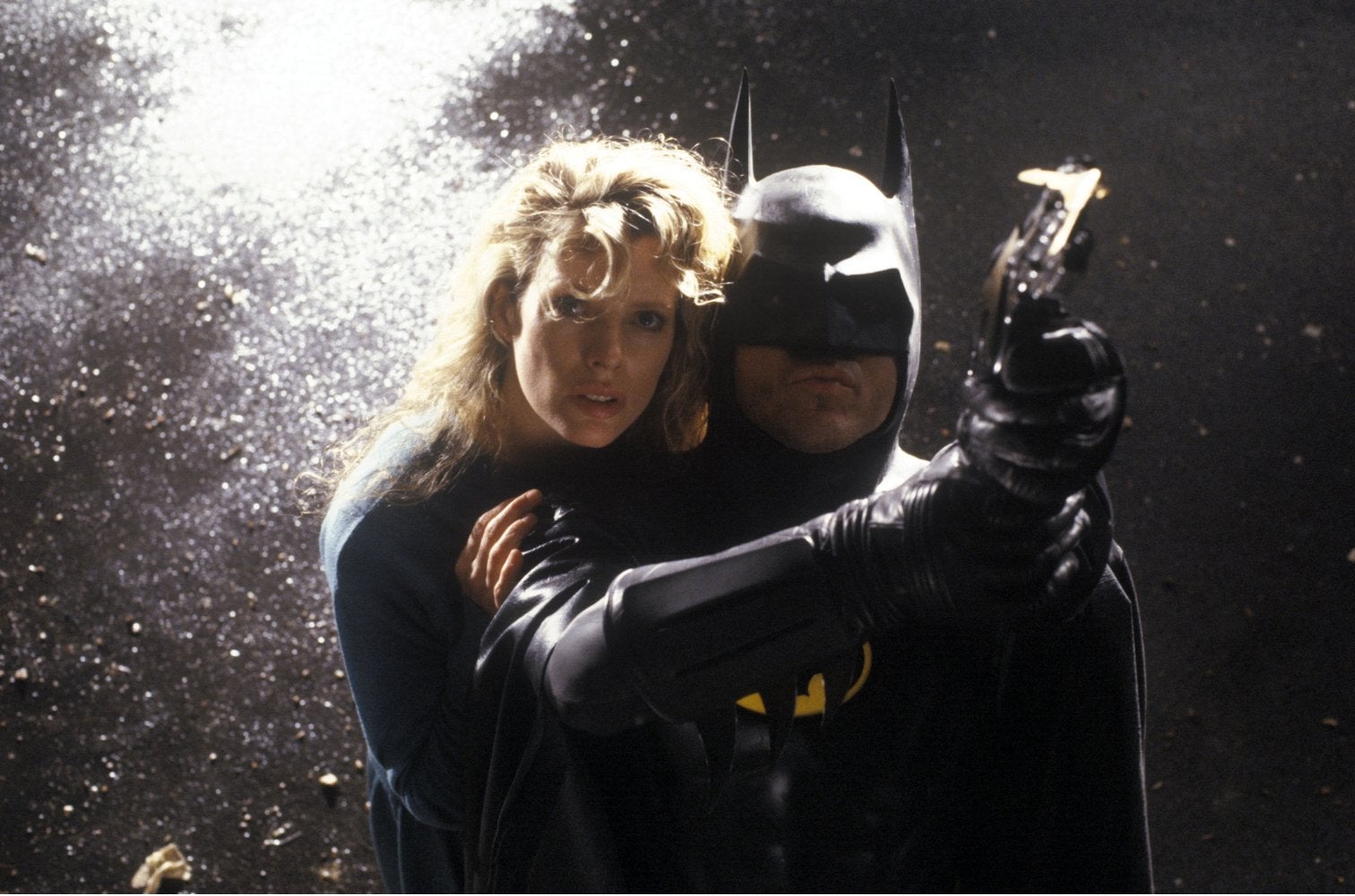 Batman is pointing a grapple-gun. A blonde woman is behind him.