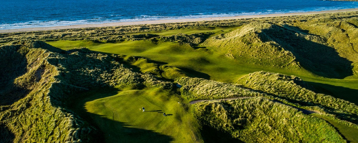 Aerial shot of a golfer on a hilly golf green with the sea in the background