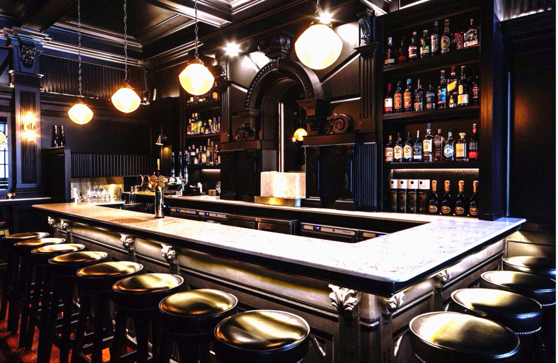 A rectangular cocktail bar surrounded by empty bar stools in a low light environment
