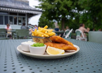 A plate of fish and chips with peas and a lemon slice