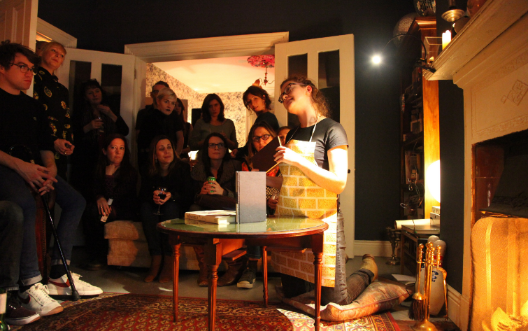 A group of people sitting around an artist as they deliver a talk in a home setting.