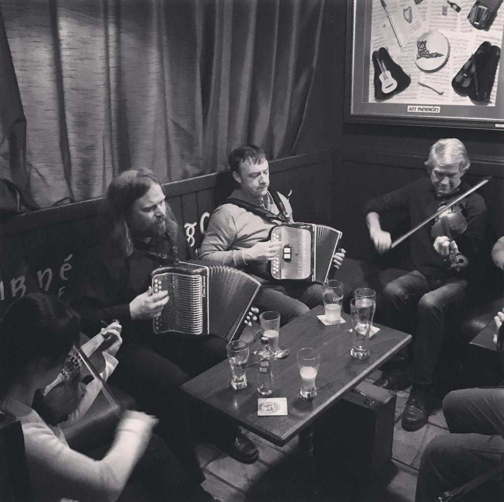 Fleadh na Bealtaine 2026 Galway - people seated playing musical instruments with table holding drinks.