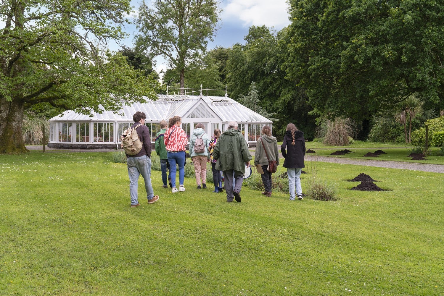 People walking across grass to an old glass house.