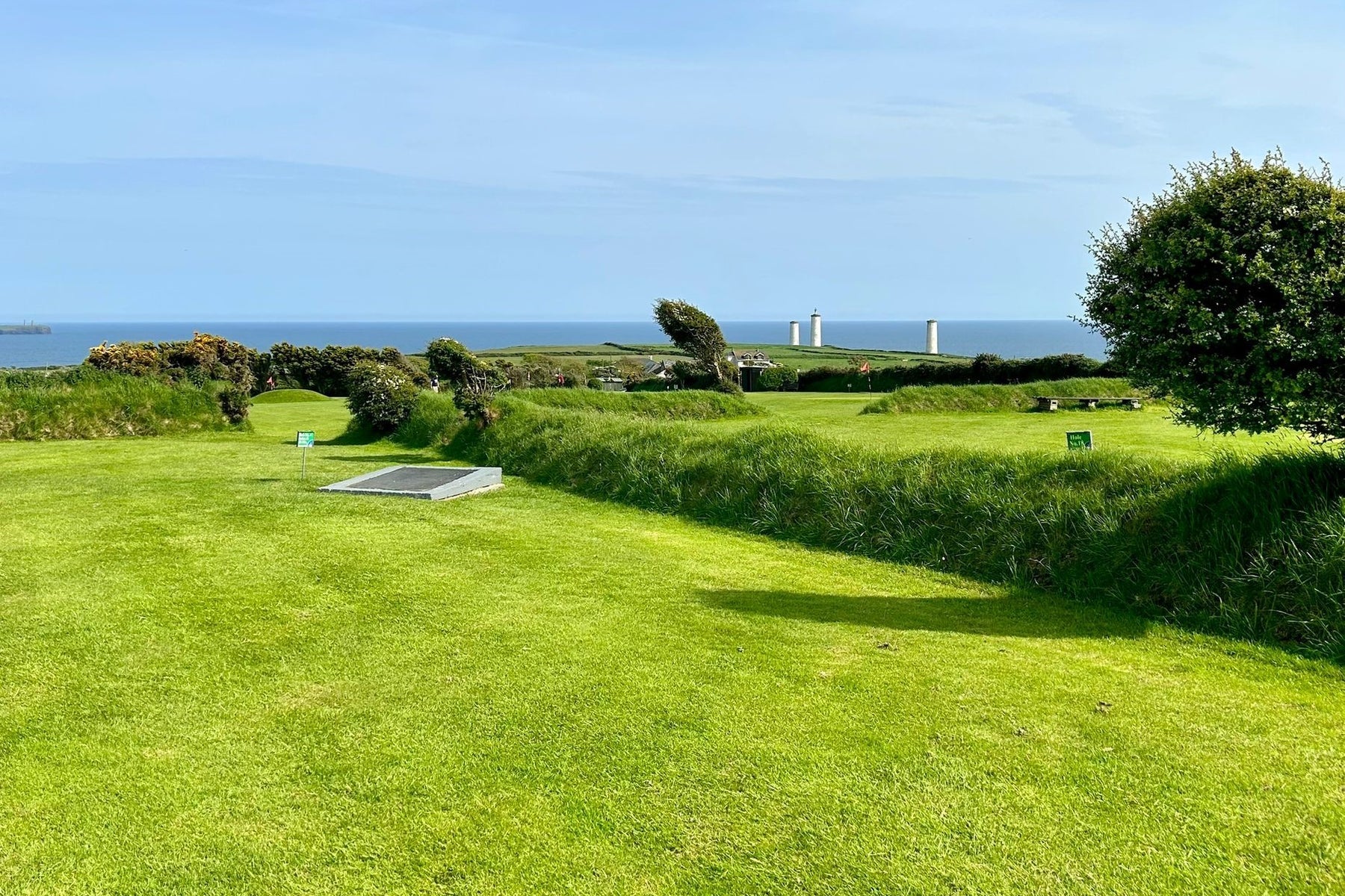 Golf green and trees with the ocean and a blue sky in the background