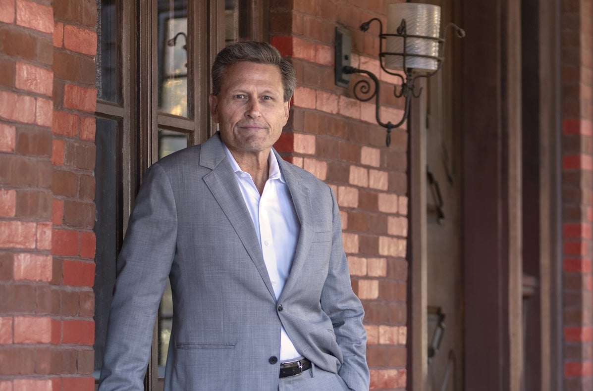 A slightly smiling man in grey jacket in front of a brick building
