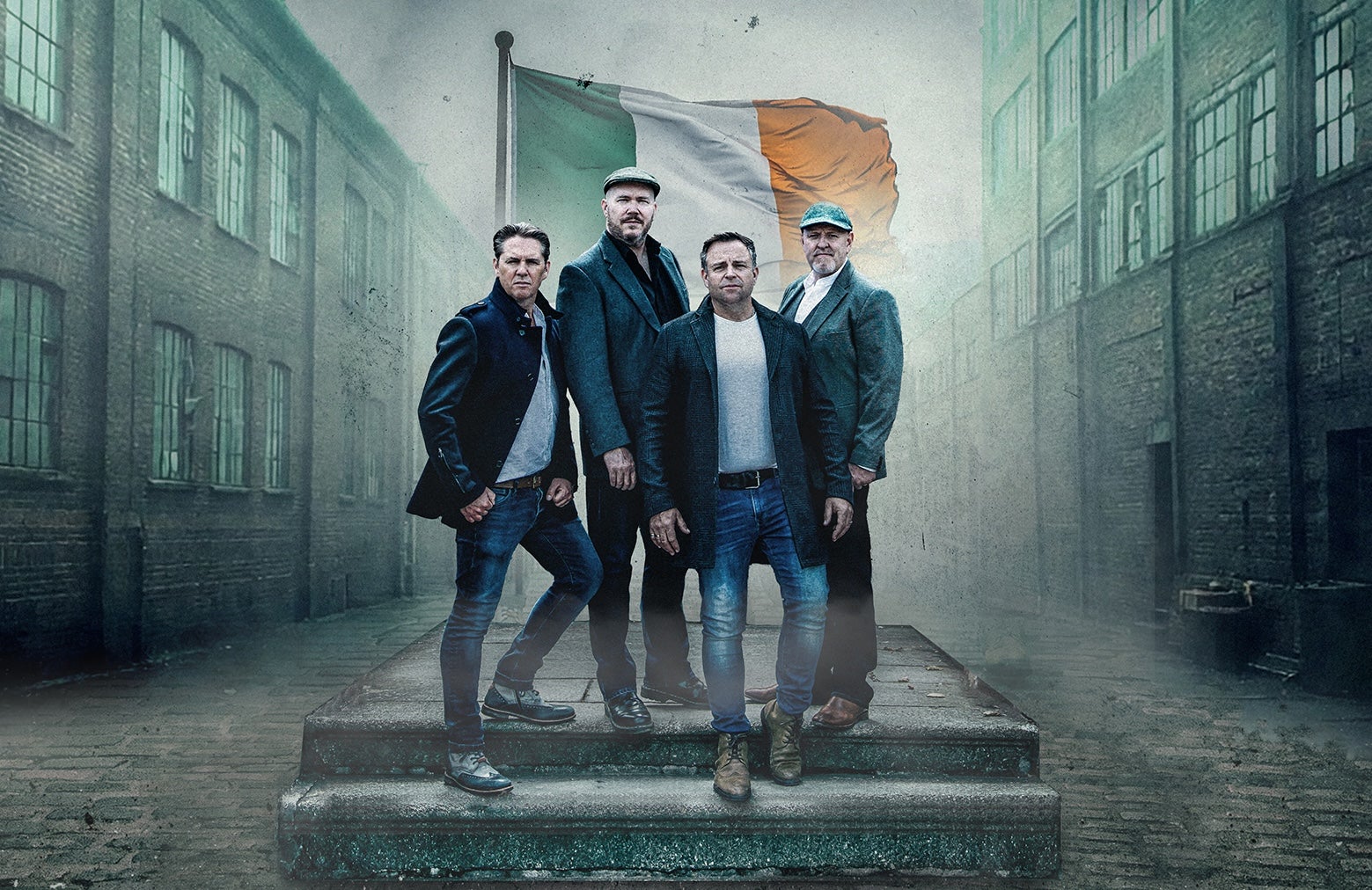 4 serious men in a group on 2 steps standing in front of Irish flag with old industrial buildings either side