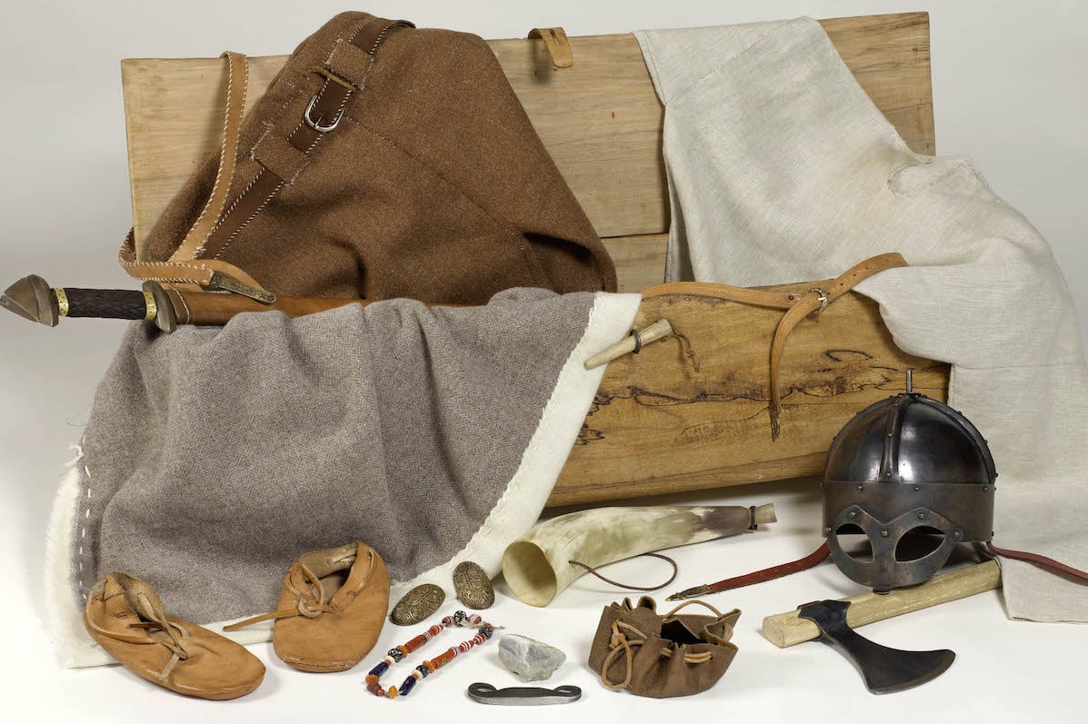 A replica Viking Chest with handmade clothes, booties and helmet with items of jewellery and axes.