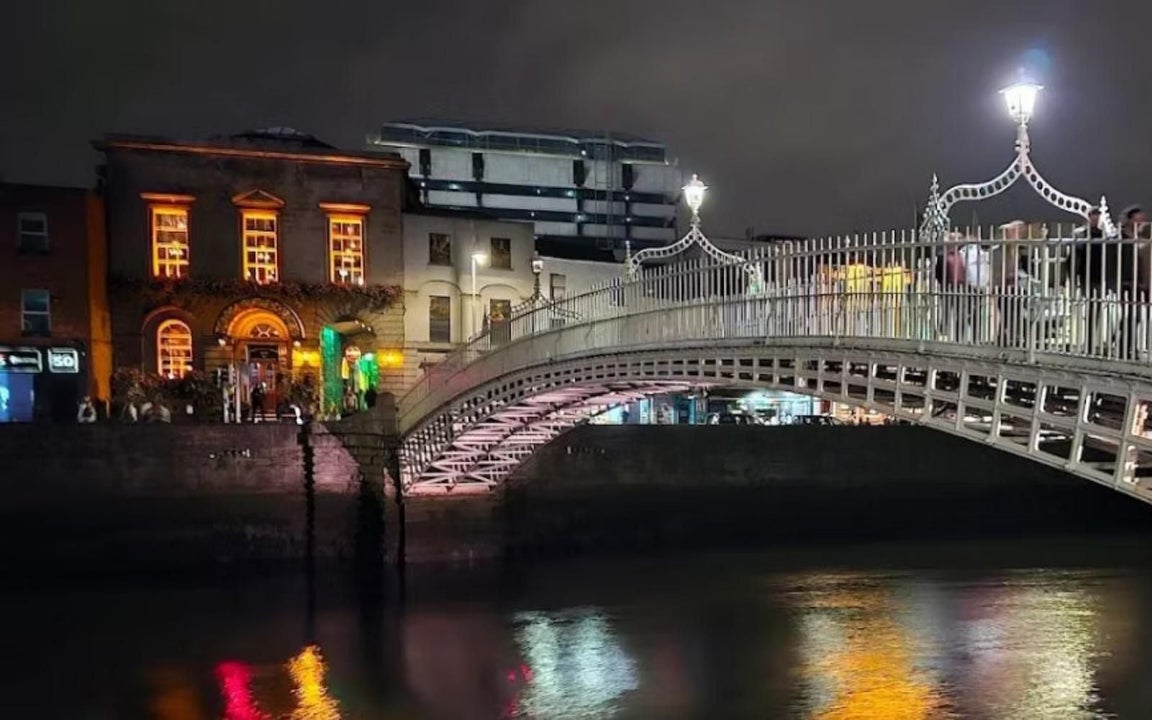 A nightscape of a bridge spanning a river with buildings on the opposite side