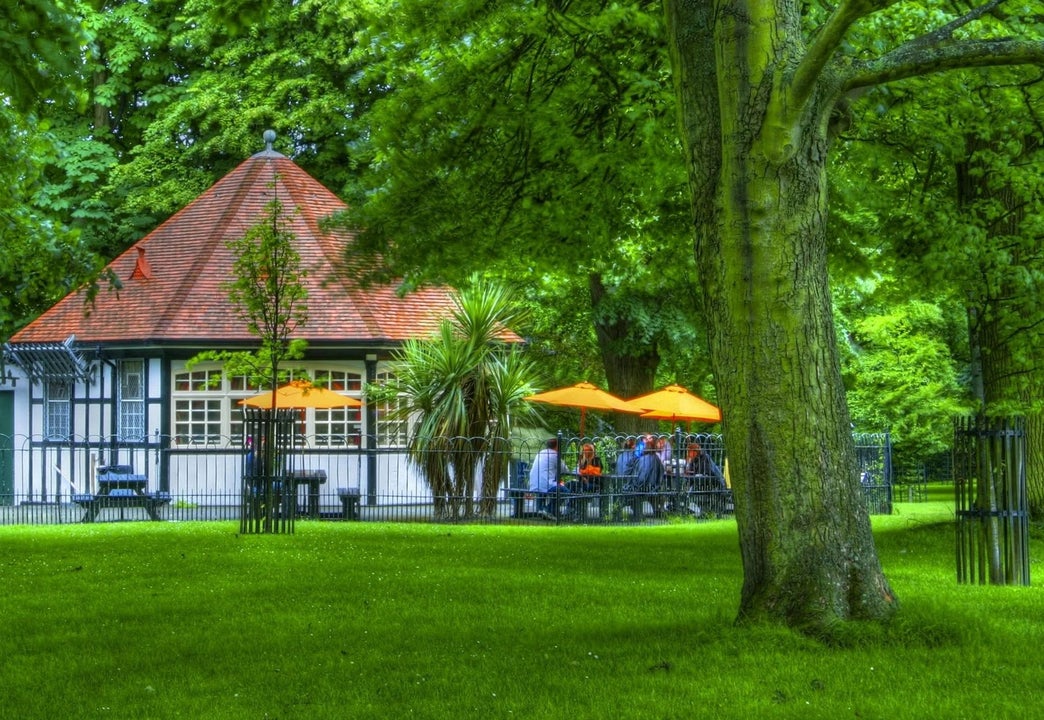 Exterior of a tea room with an outside seating set on parkland surrounded by trees
