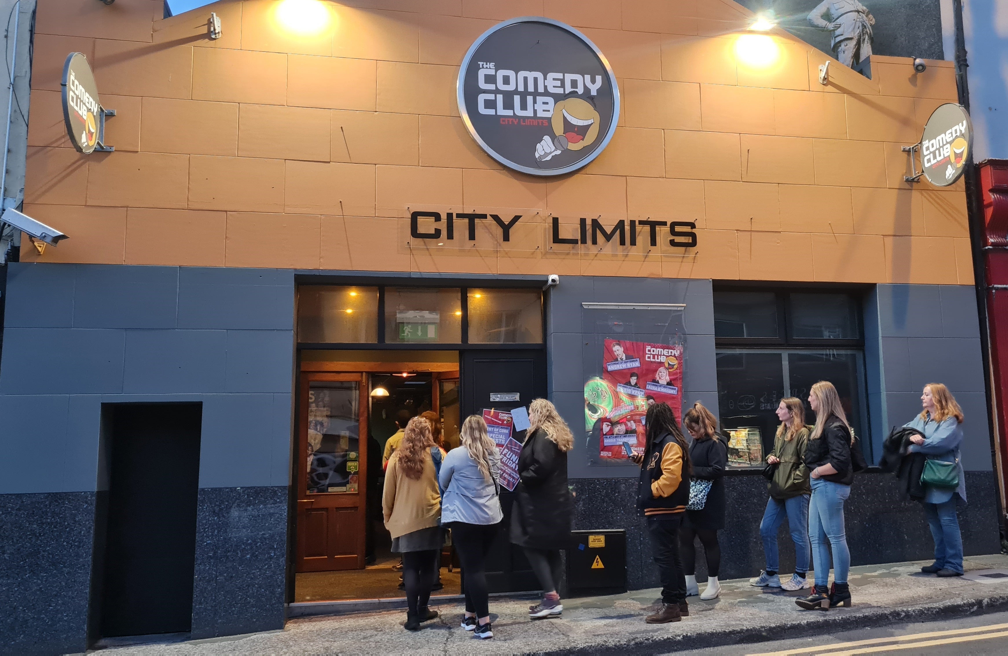 A group of people waiting outside a grey and yellow building.