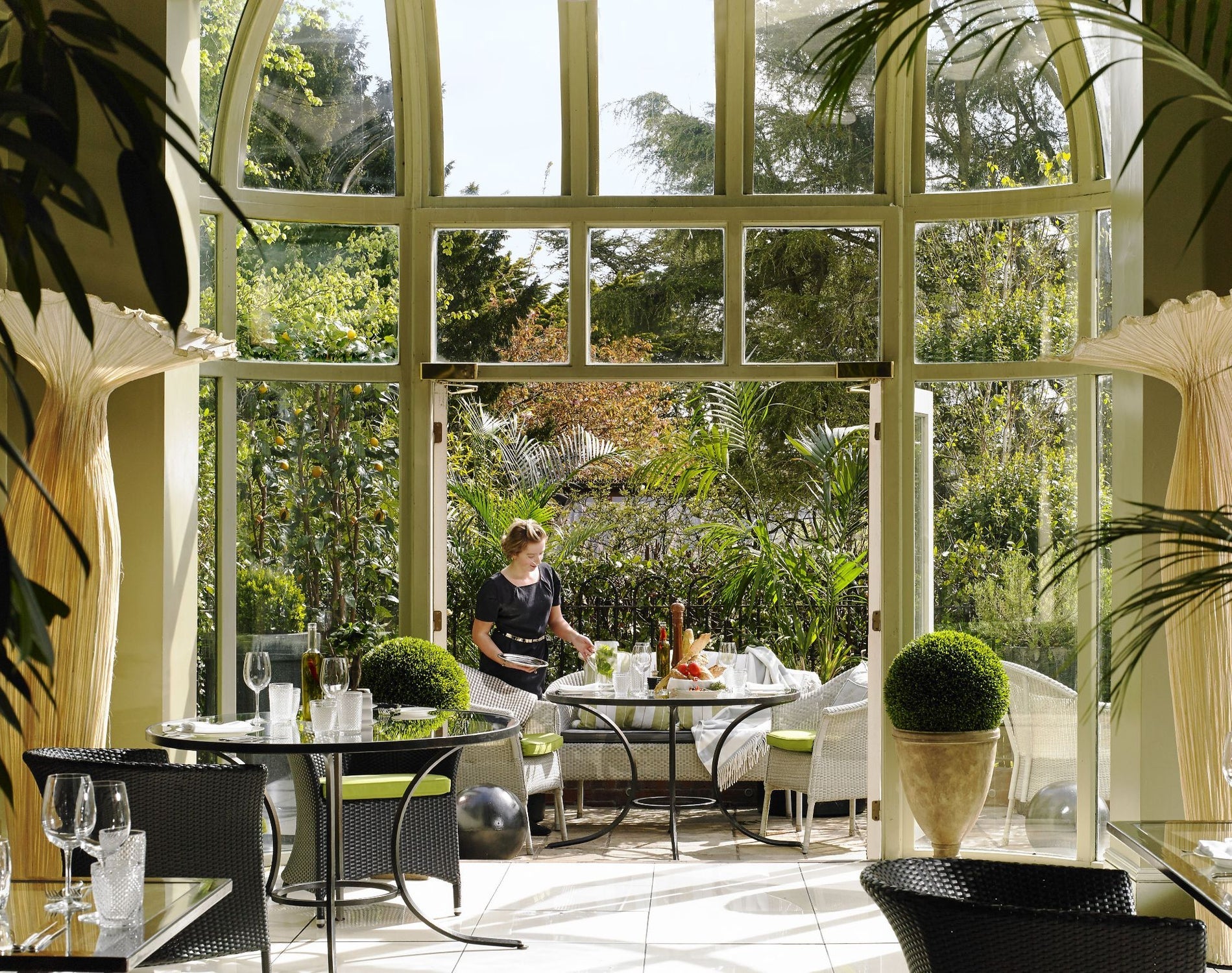 Garden view restaurant with a staff member setting a table beside large open windows