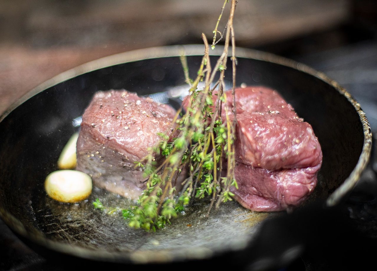 Two steaks with garlic and herbs in a hot pan