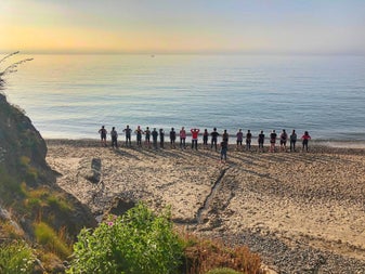 A group standing on sand by the sea watching the sunrise in the distance