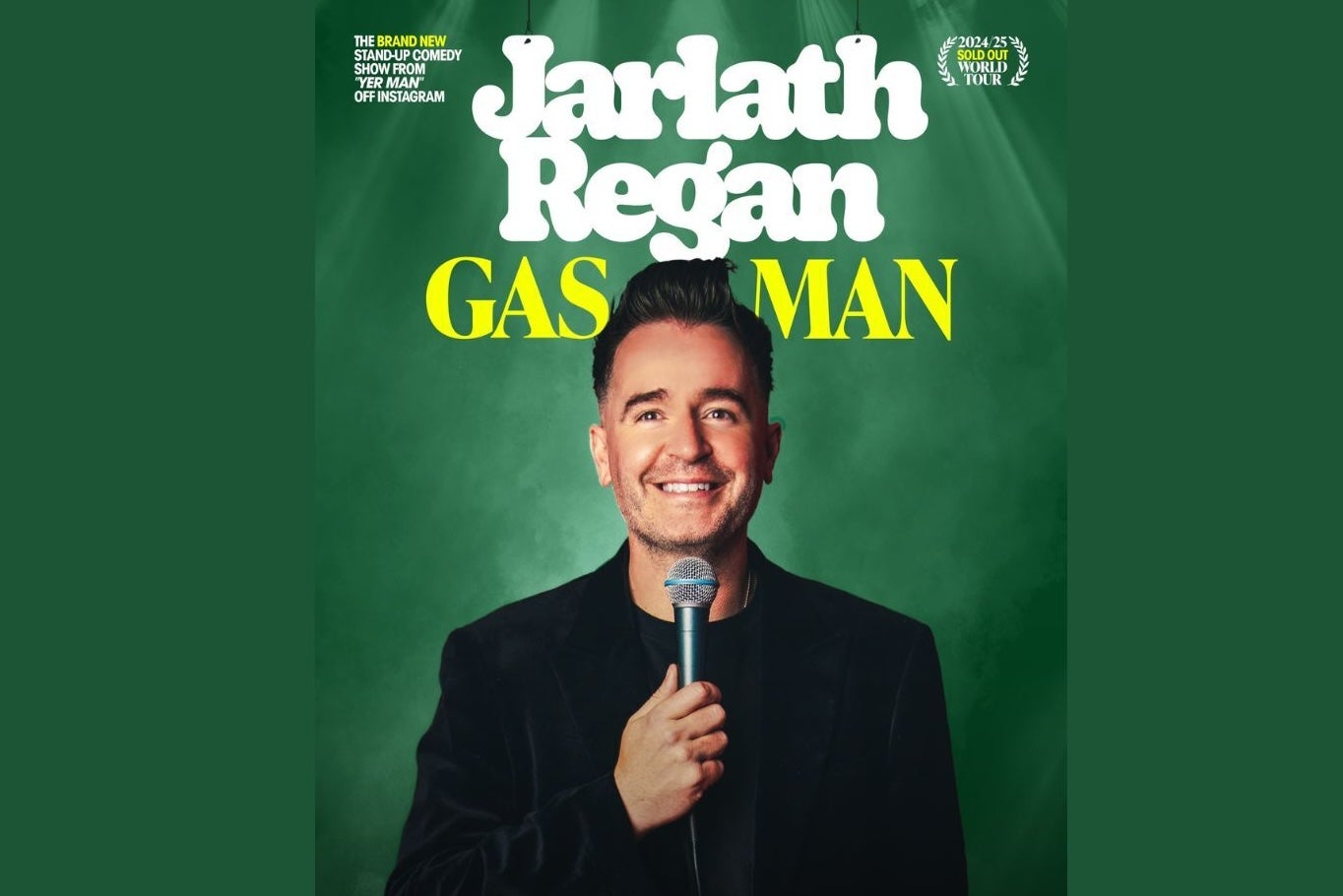 Man dressed in black, smiling holding a mic up to his face, against dark green background.