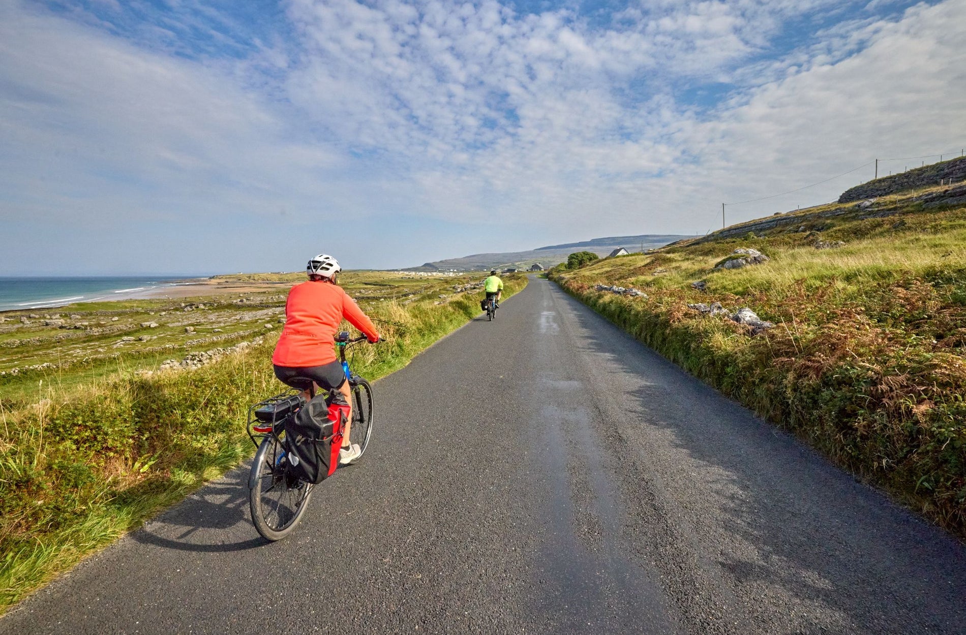 Two cyclists on a country road lined with stone walls and a coastal view