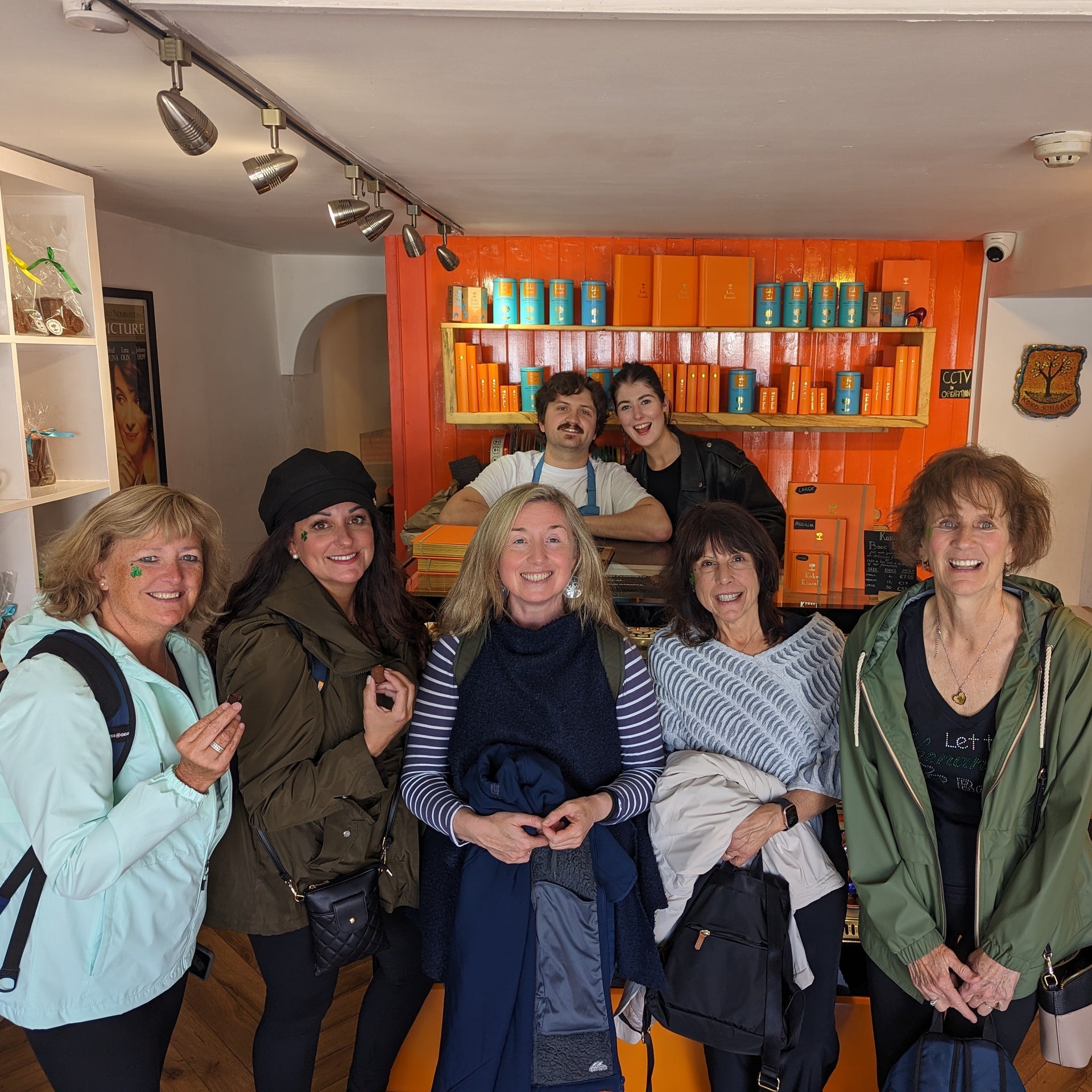 Group of people smiling for a picture with a shelf displaying chocolate and an orange wall in the background
