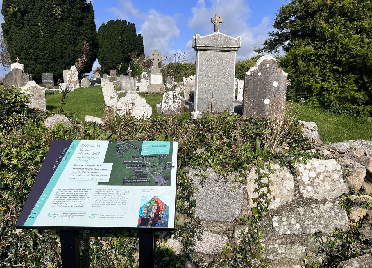 View over wall of a cemetery with a story board and old headstones