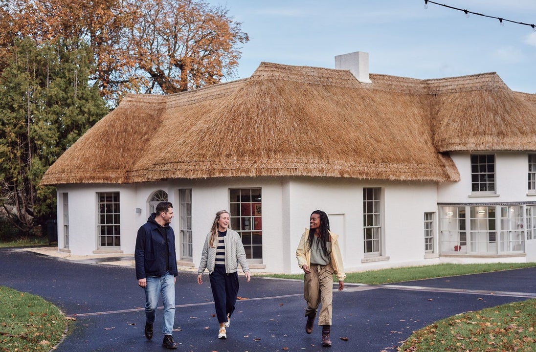 Three people walking away from a white building with a thatched roof