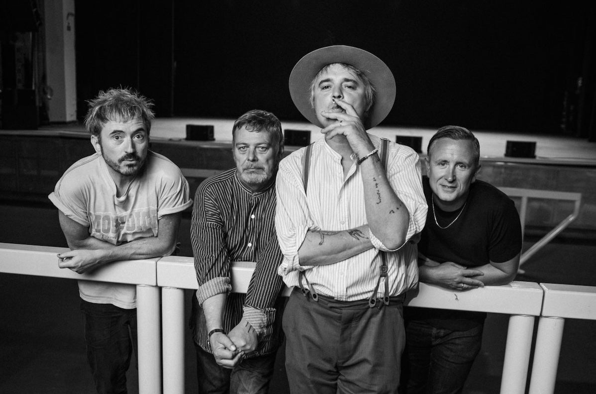Black and white photo of 4 men leaning on or against a thick rail