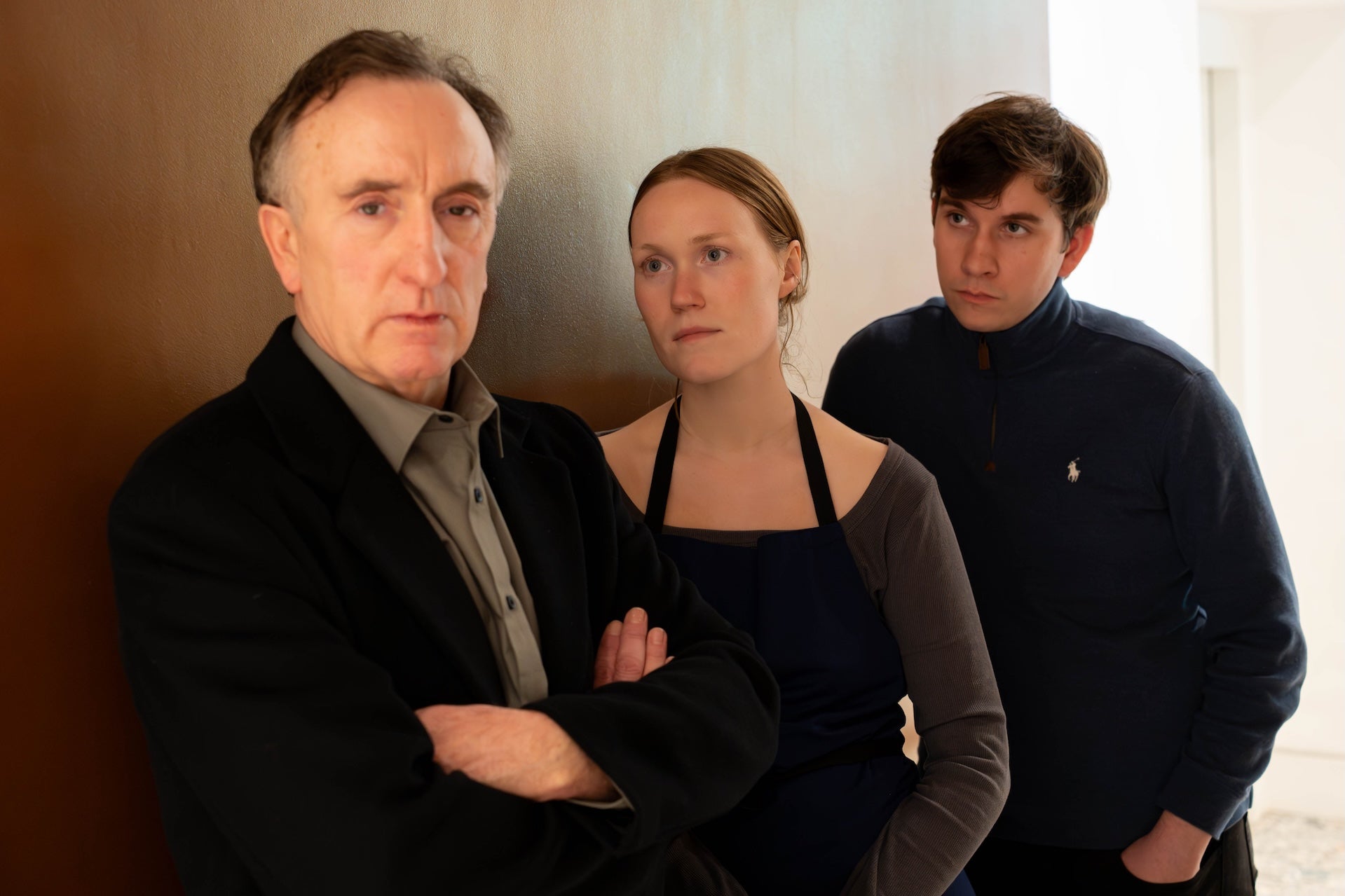 All leaning against an internal wall, 2 people are looking at a man with crossed arms, not looking at them.