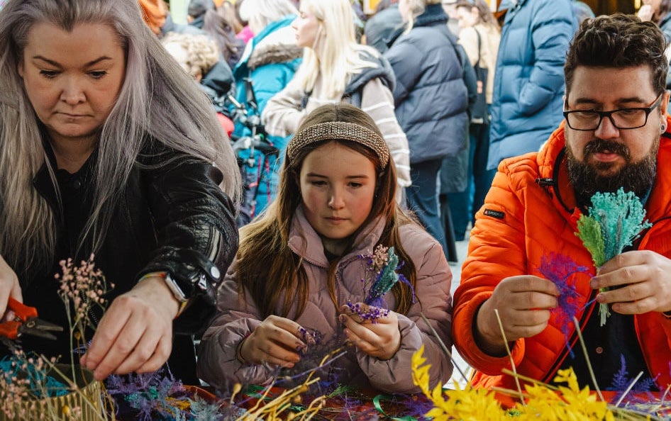 Brigit's 2026: Imbolc Fair - 2 adults and a child concentrating on arranging dried flowers.
