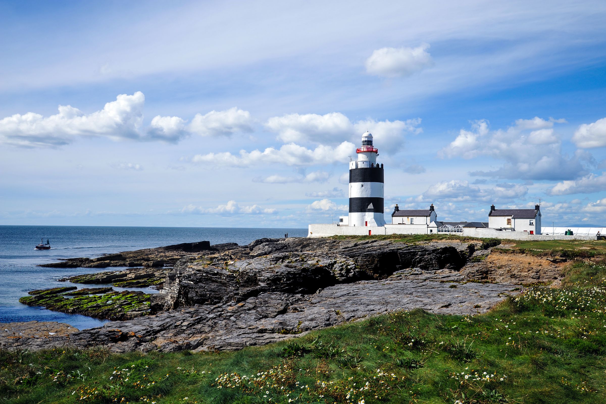 Hook Head Lighthouse beside the sea in Wexford surrounded by rocks and grass.