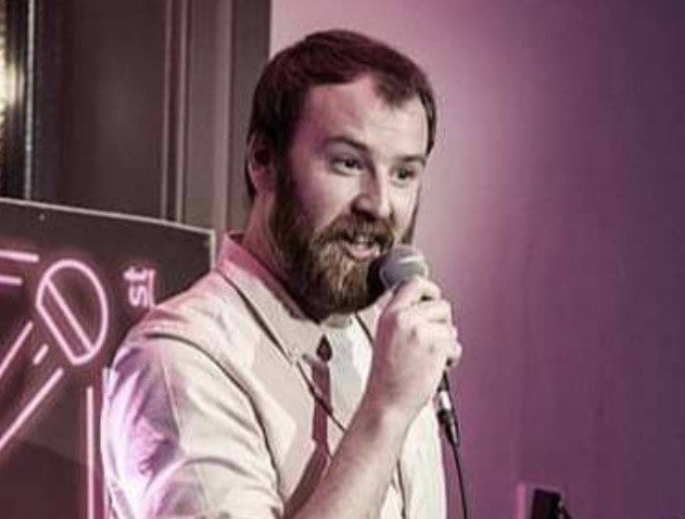 A man with a beard holding a mic, talking