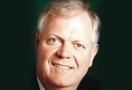 A gentle smiling man against plain dark background.