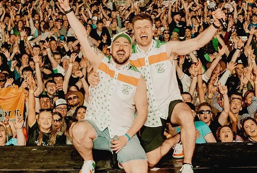 2 men kneeling down, shouting and waving arms in the air with a large waving crowd behind them