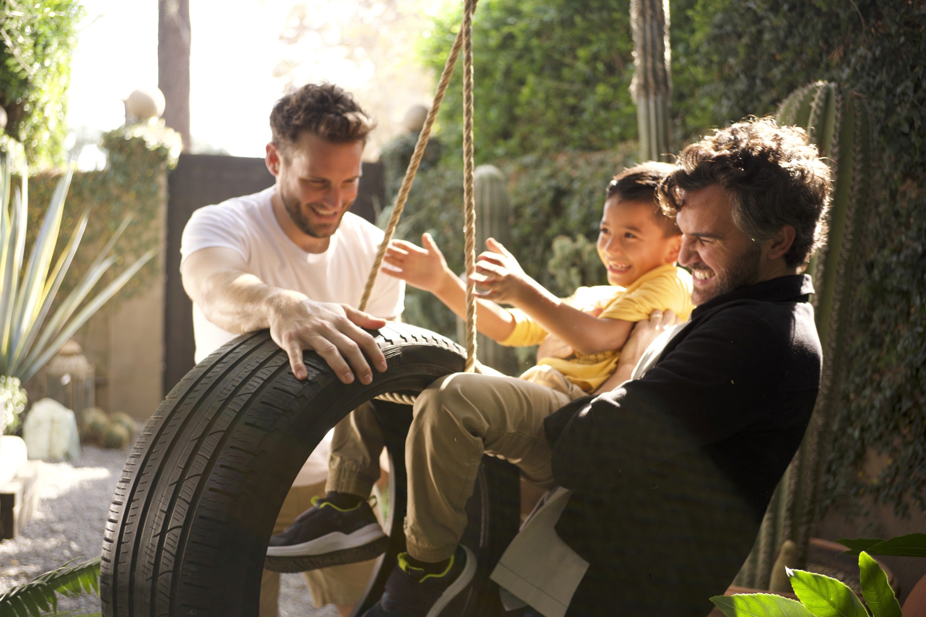 Two men and a boy are playing with a tyre swing.