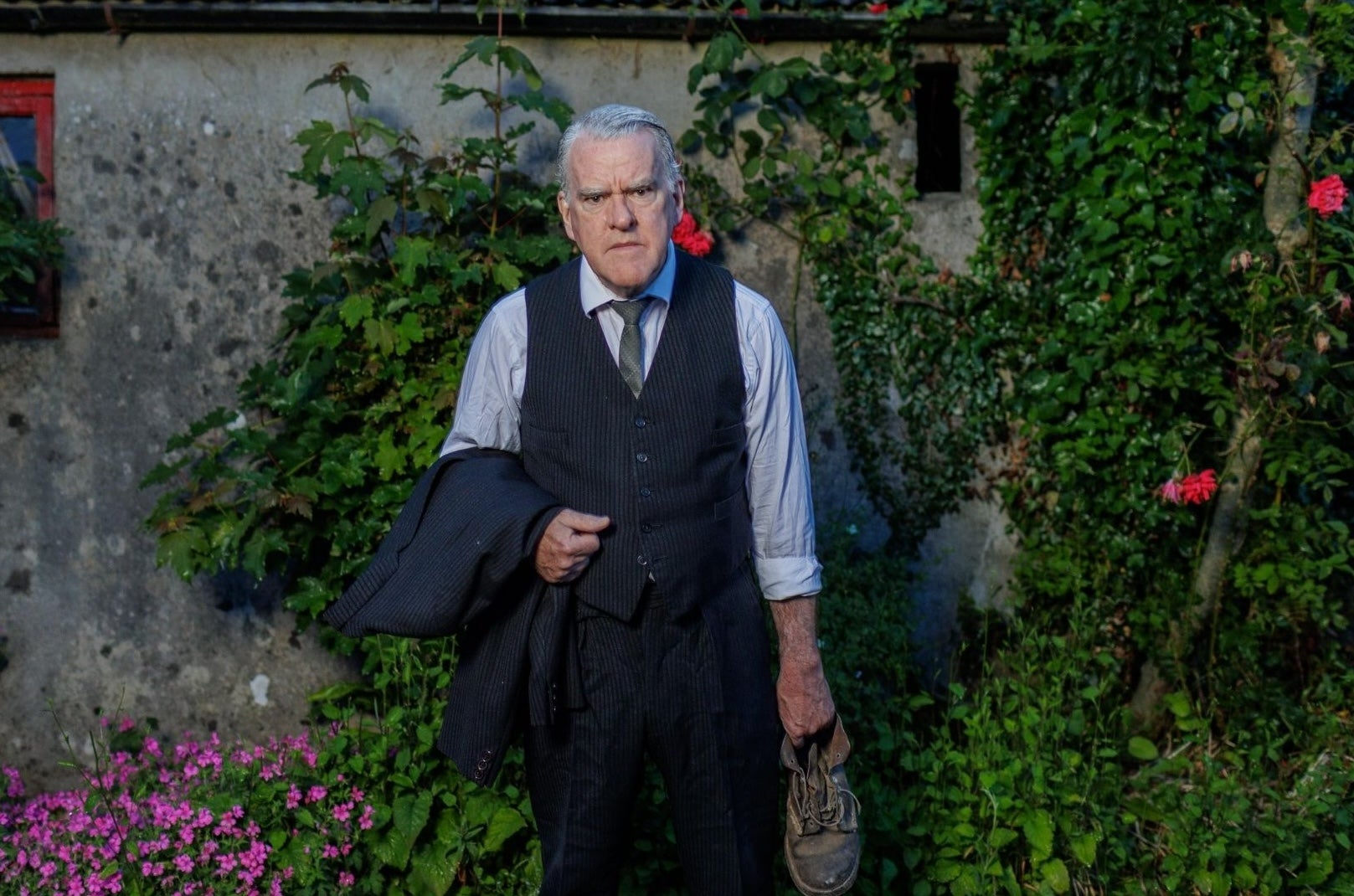 The Man In The Woman’s Shoes at Backstage - a grumpy looking man in shirt and tie holding a jacket in one hand and an old shoe in the other.