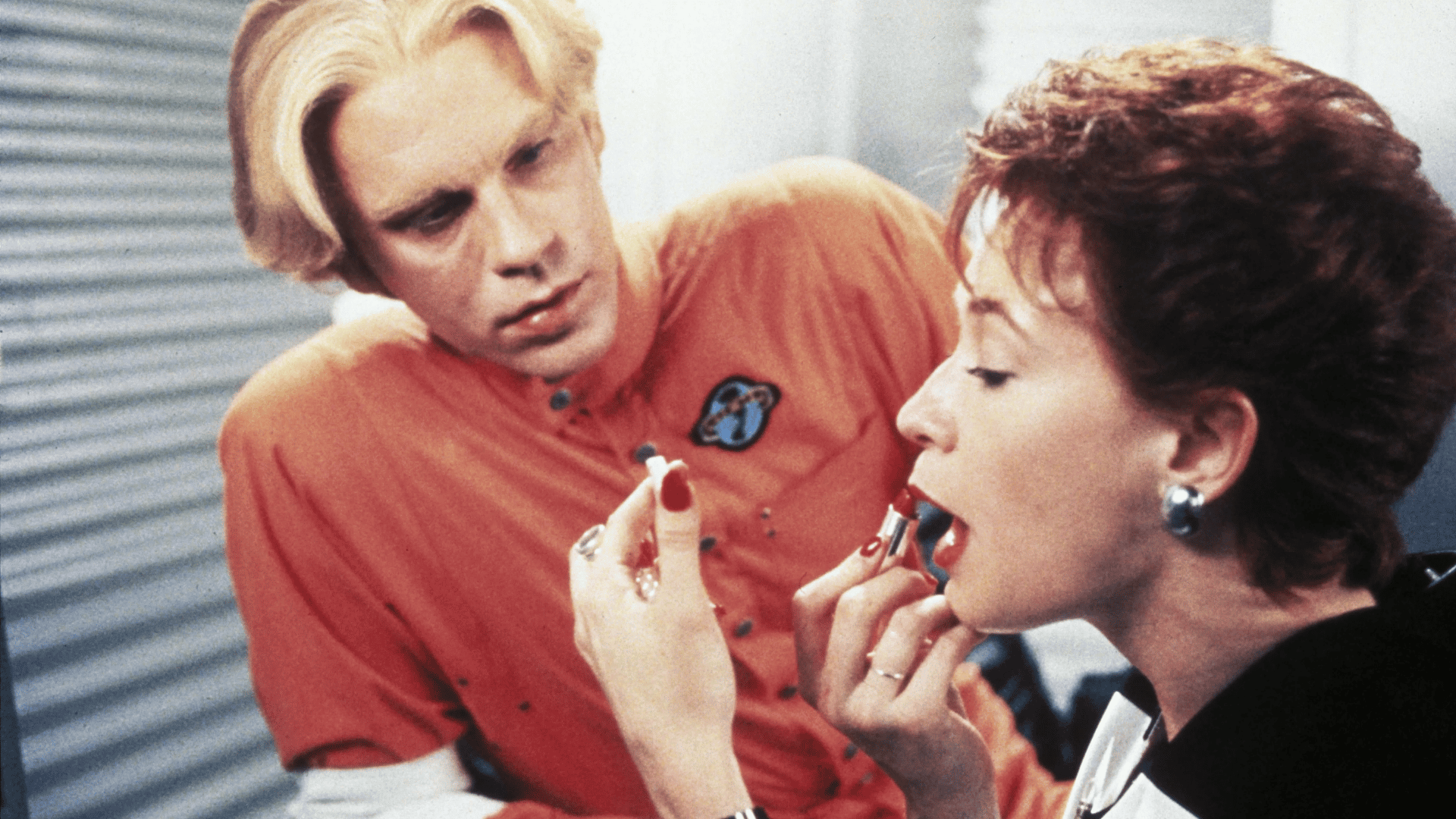 A man looking at a woman putting on lipstick.