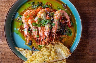 Prawns surrounded by oil on a blue plate with two slices of bread on the edge
