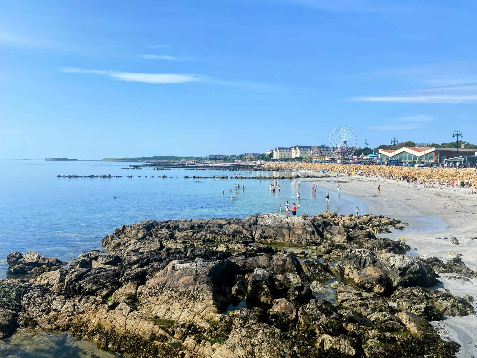 View from the rocks towards a beach with a town and ferris wheel in the background