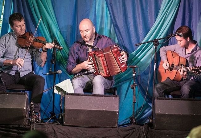 Joyce Brothers Music Festival 2026, 3 seated musicians playing instruments on a small stage area.