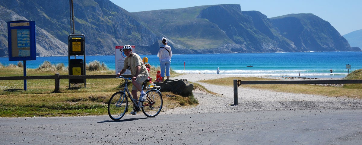 A cyclist at an entrance to a beach with mountains in the background