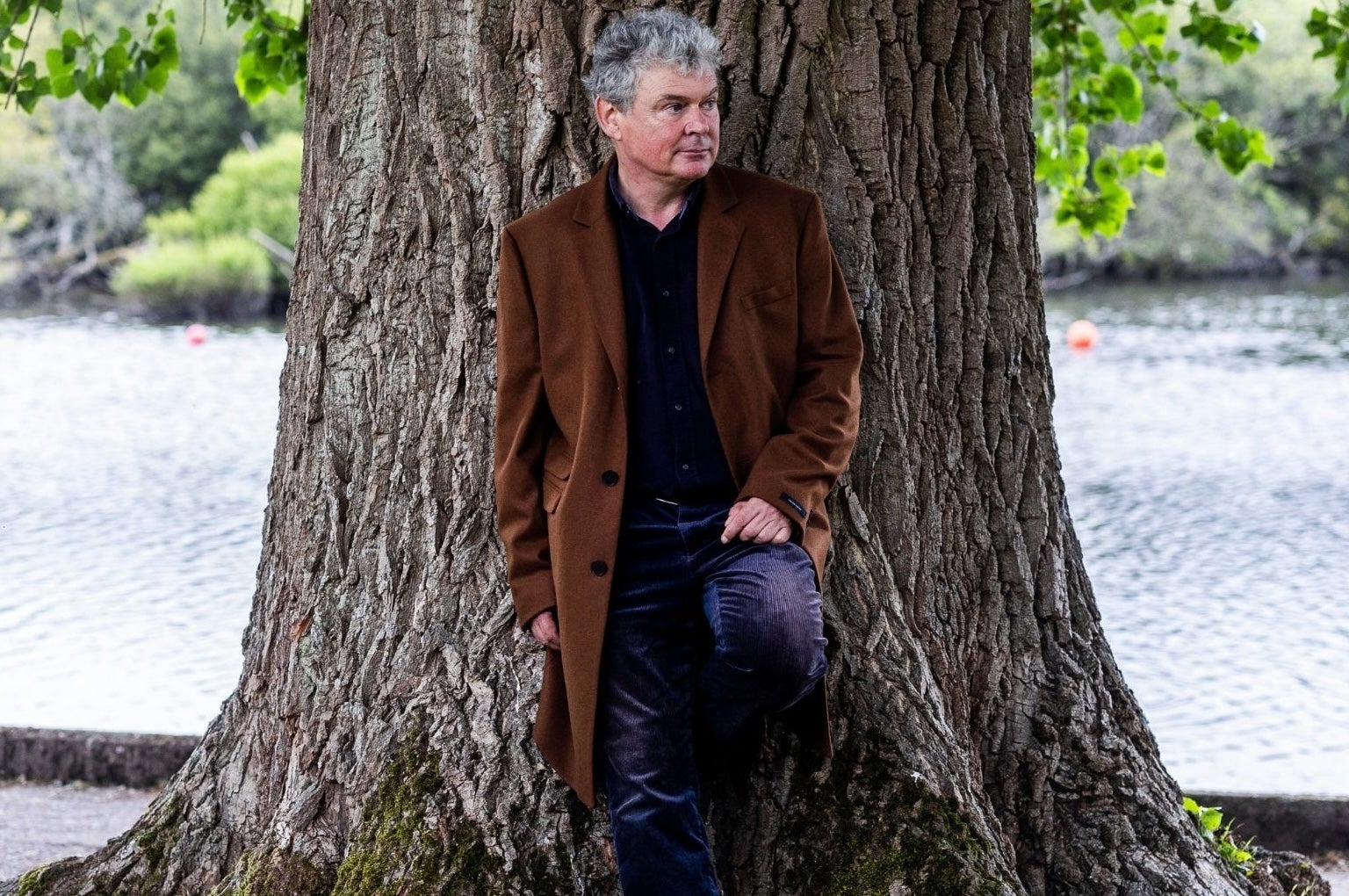 John Spillane standing against a tree by a river.