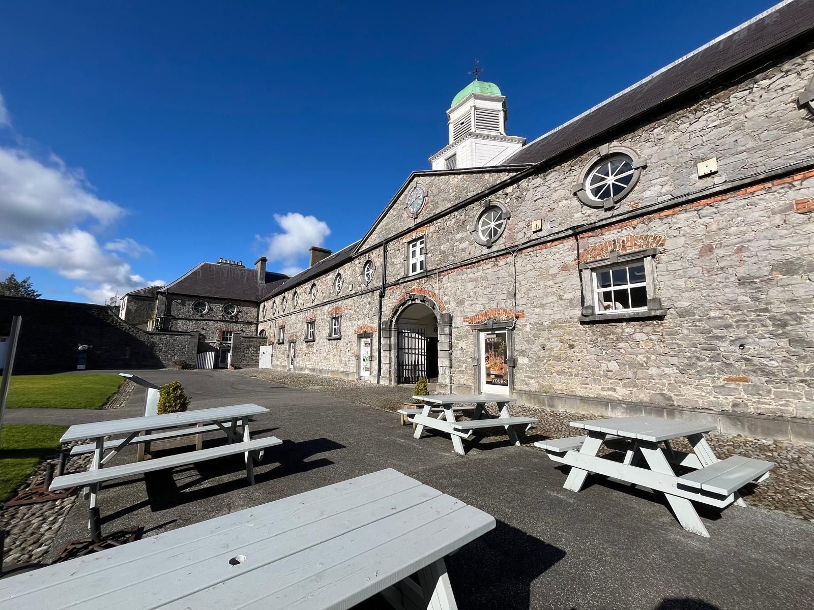 Four picnic benches on a paved area outside a big stone building