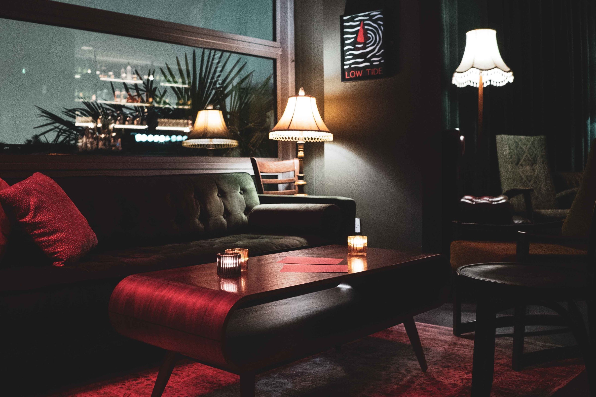 Dark coloured sofa and seating area with muted red coloured accessories and menus on a low table.