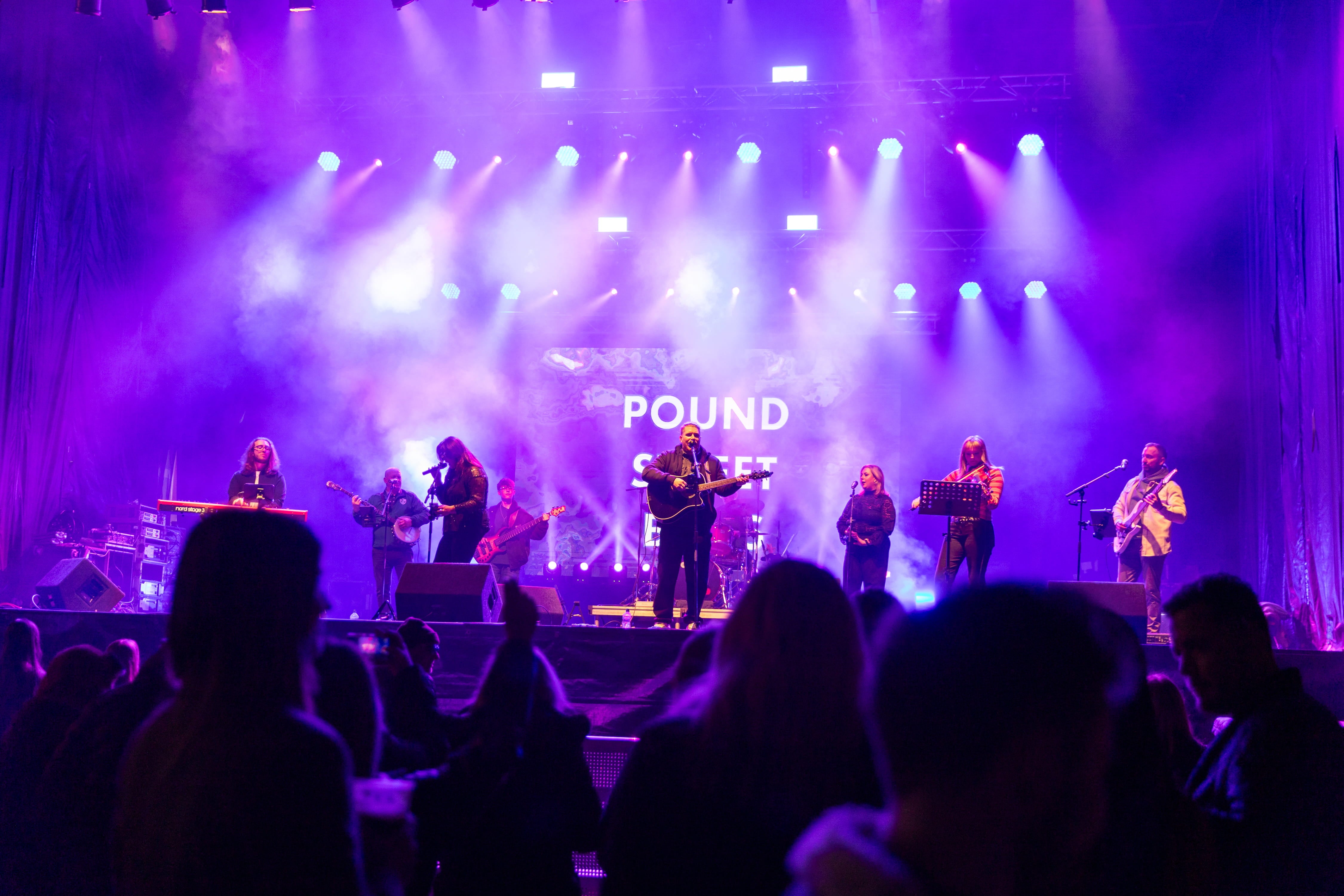 View of a band playing on a stage with purple and white lights.