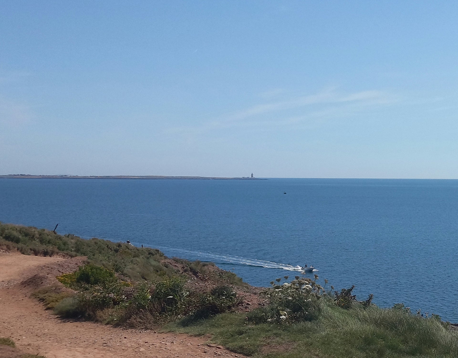 Boat in sea beneath Dunmore East cliffs with Hook Lighthouse in the distance