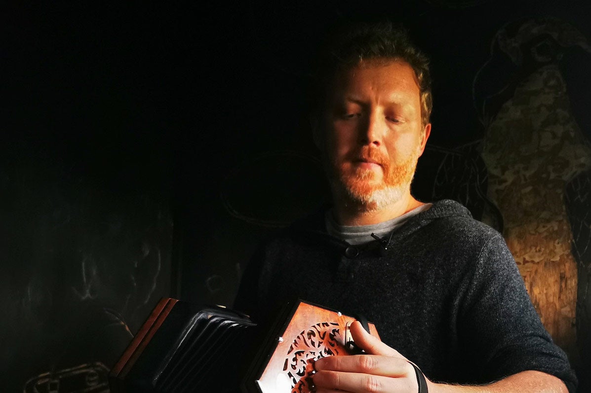 Cormac Begley - Gleneagle, a man looking down at a small hand accordion he is playing.