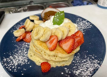 A plate of American style pancakes with whipped cream bananas and strawberries at Sweet Churro