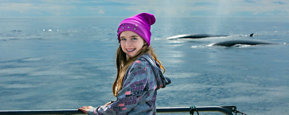 Image of girl on a boat with two dolphins in the background