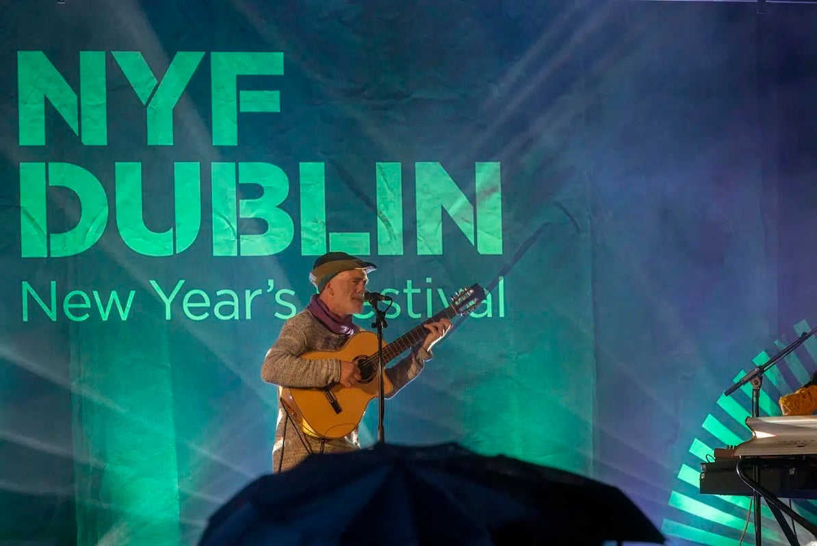 NYF Dublin, Traditional Music Concert - a man playing a guitar and singing on a stage, lit behind in green