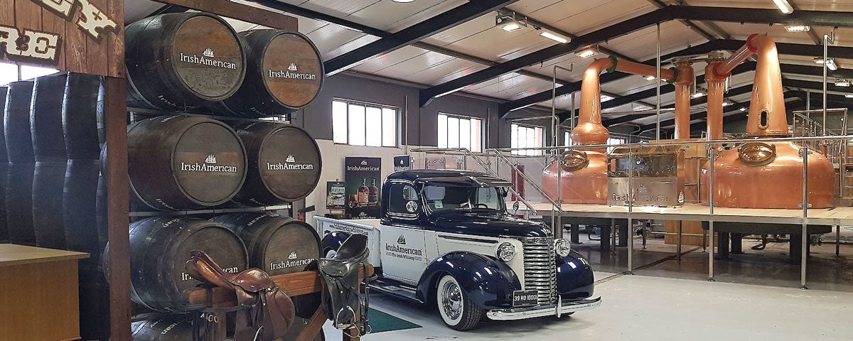 Vintage American car set against the backdrop of the copper distilling pots and stacked whiskey barrels